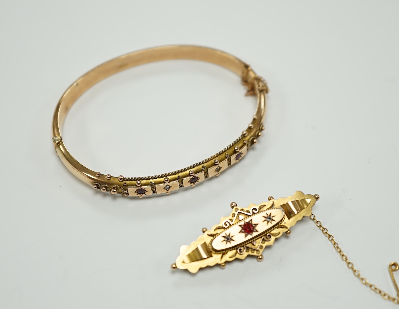 An Edwardian 9ct gold ruby and diamond chip set hinged bangle and a similar yellow metal, ruby and diamond chip set bar brooch, gross weight 12.1 grams.